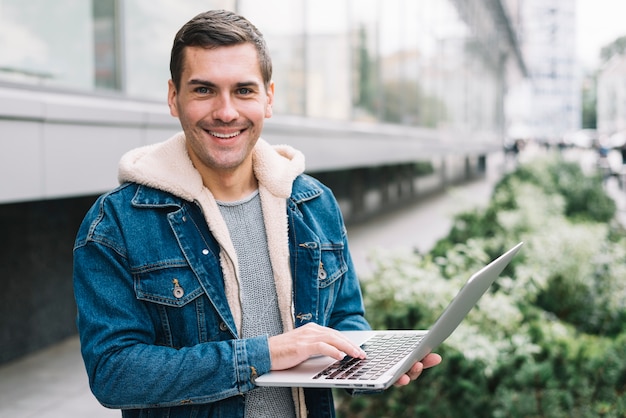 Gratis foto moderne mens die laptop in stedelijke omgeving met behulp van