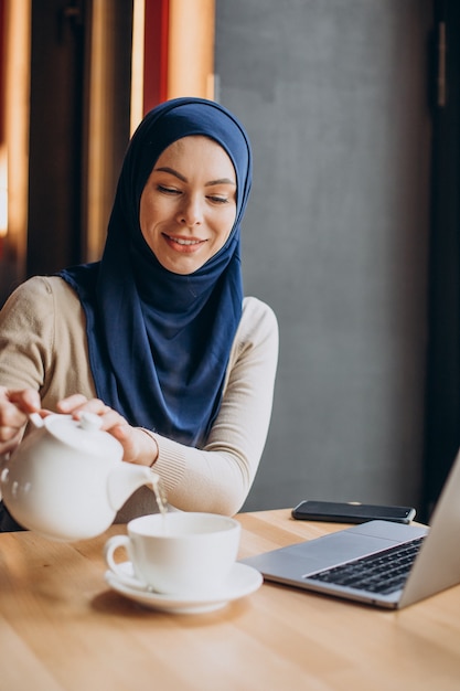 Moderne moslimvrouw die thee drinkt en op de computer werkt in een café