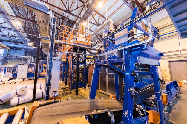Moderne operationele fabrieksapparatuur die glasvezel produceert met rollen steenwol of glaswol op de achtergrond zware industrie machines metaalbewerking werkplaatsconcept