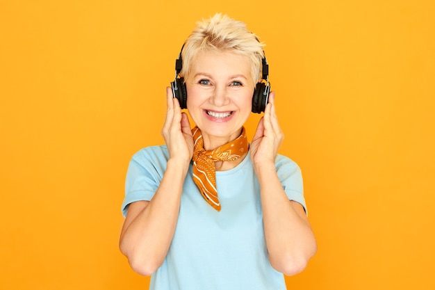 Moderne stijlvolle blanke vrouw gepensioneerde m / v met korte haarstijl ontspannen luisteren naar favoriete nummers via oordopjes. Aantrekkelijke rijpe vrouw genieten van mooie muziek met behulp van draadloze Bluetooth-koptelefoon