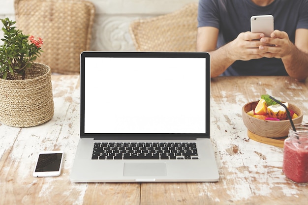 Moderne technologie, zaken en communicatie. Werkruimte met opengeklapte laptop pc, mobiele telefoon en voedsel op houten tafel. Notebook-computer met een leeg wit scherm voor uw ontwerp