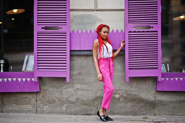 Modieus Afrikaans-Amerikaans meisje met roze broek en rode dreadlocks poseerde buiten