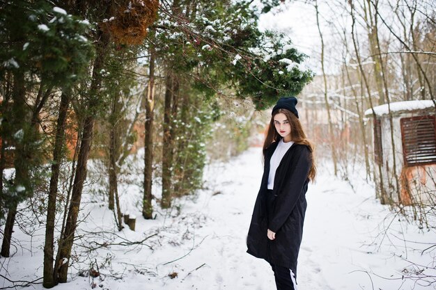 Modieus brunette model met lange benen in lange zwarte mantel en hoed buiten op winterdag