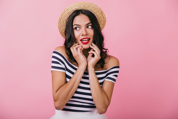 Modieuze blanke vrouw met een gebruinde huid poseren met oprechte emoties. Portret van elegant krullend meisje in hoed.