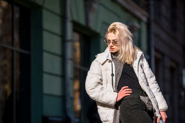 Modieuze blonde jonge vrouw die in openlucht stellen