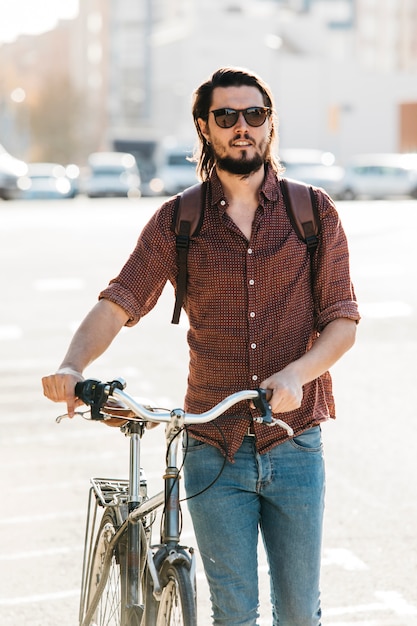 Gratis foto modieuze jonge mens die met fiets op weg loopt