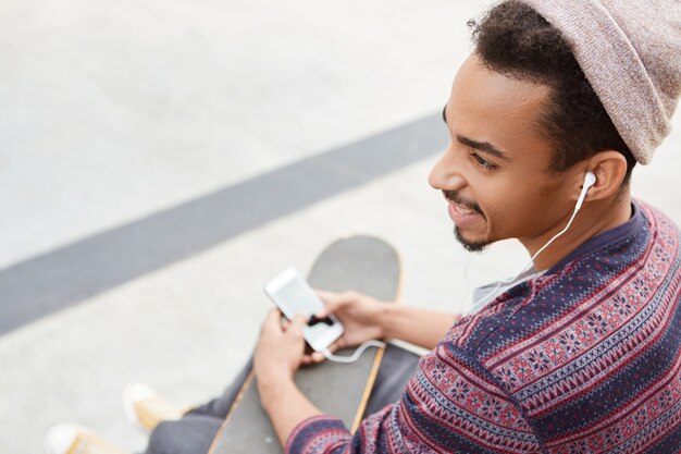 Modieuze jongere met een donkere huid draagt een trendy hoed en shirt, geniet van het favoriete muziekgenre,