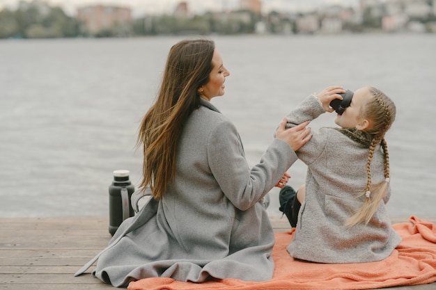 Modieuze moeder met dochter. Mensen op een picknick. Vrouw in een grijze jas. Familie aan het water.