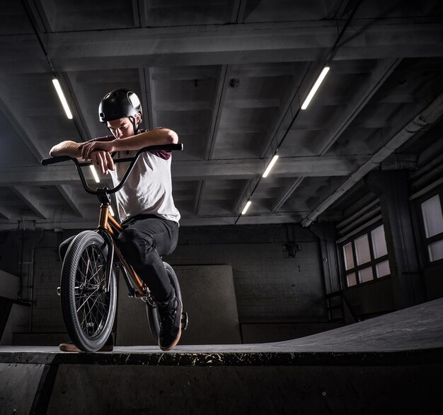 Moe BMX-rijder in beschermende helm zittend op zijn fiets in een skatepark binnenshuis