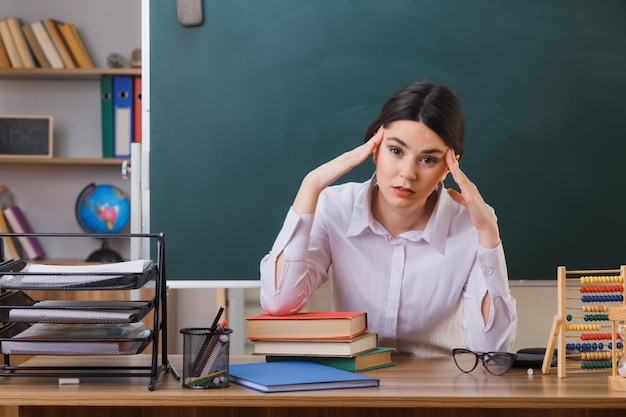 moe greep het hoofd van een jonge vrouwelijke leraar die aan het bureau zit met schoolhulpmiddelen in de klas