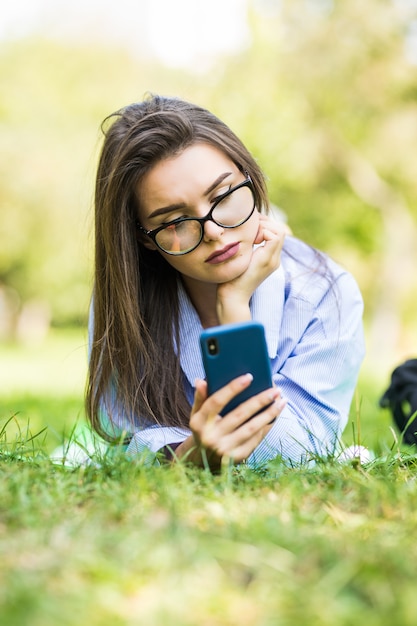 Moe jonge hipster meisje met behulp van slimme telefoon liggend op het gras in het park