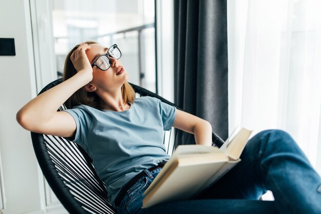 Moe jonge vrouw met boek slapen op lounge stoel thuis