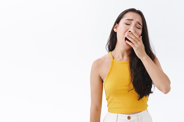 Moe of verveeld aantrekkelijke stijlvolle brunette Oost-Aziatische vrouw uitgeput van oninteressant gesprek in slaap vallen van verveling geeuwen tilt hoofd en dekking geopende mond staan witte achtergrond