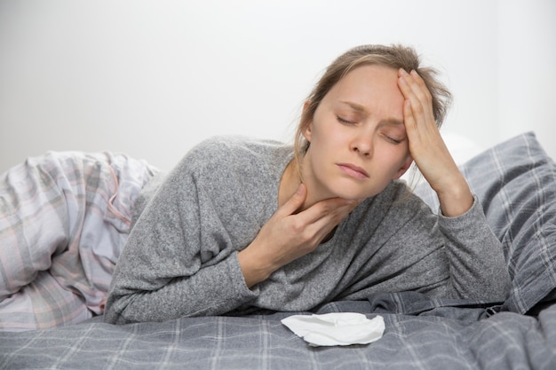 Moe zieke vrouw in bed met gesloten ogen met zere keel