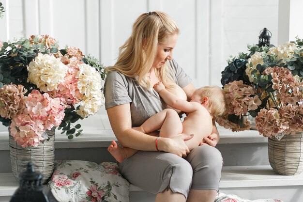 Moeder die baby op haar overlappingen vóór het de borst geven houdt. Studio opname in bloemen decor