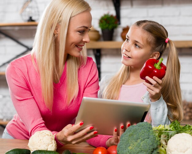 Moeder die een digitale tablet en een dochter houdt die paprika houdt