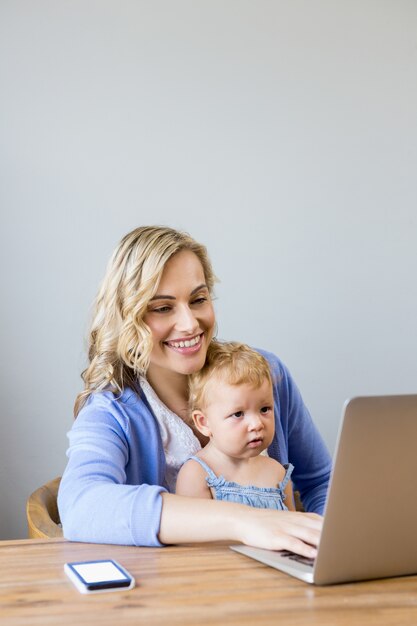 Moeder en baby zitten aan tafel en met behulp van laptop