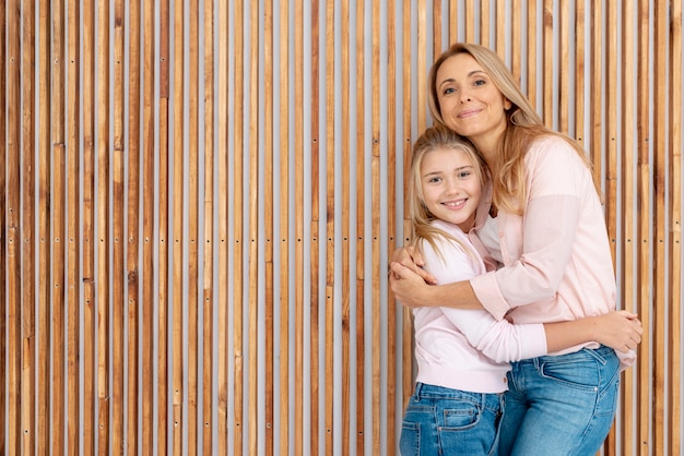 Moeder en dochter die naast houten achtergrond omhelzen