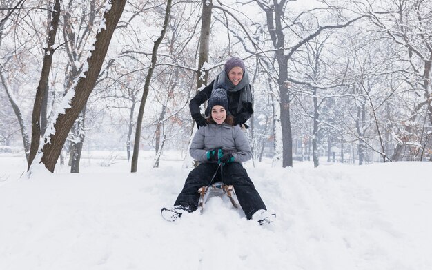 Moeder en dochter die van sleerit genieten in bos bij de winterdag