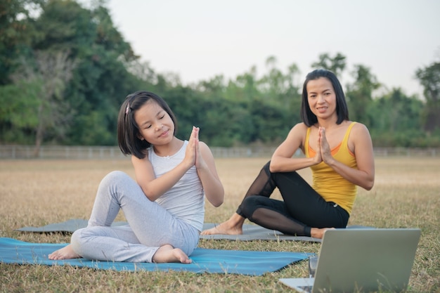 Moeder en dochter doen yoga. vrouw en kind training in park. buitensport. gezonde sportlevensstijl, kijken naar yoga-oefeningen online video-tutorial en stretchen in ardha matsyendrasana pose