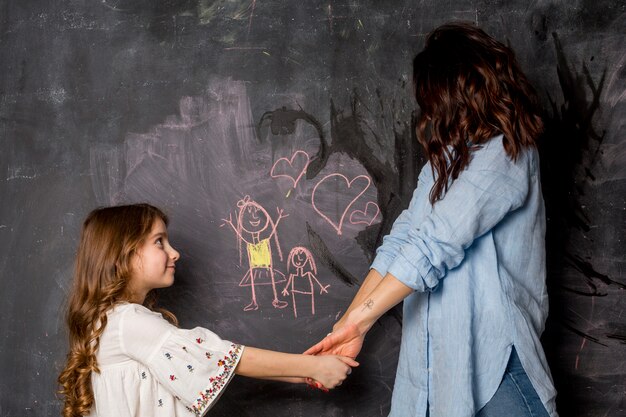 Moeder en dochter hand in hand in de buurt van schoolbord met tekening