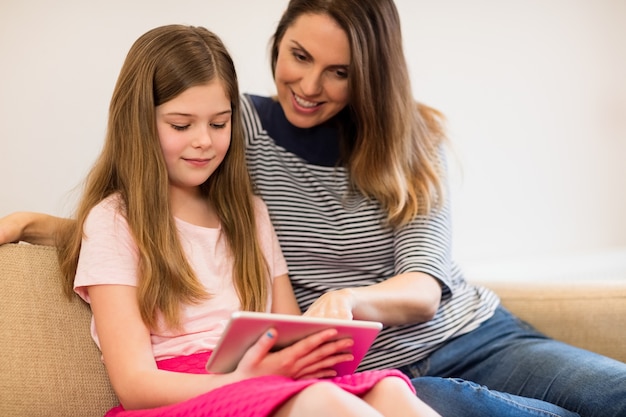 Moeder en dochter met behulp van digitale tablet in woonkamer