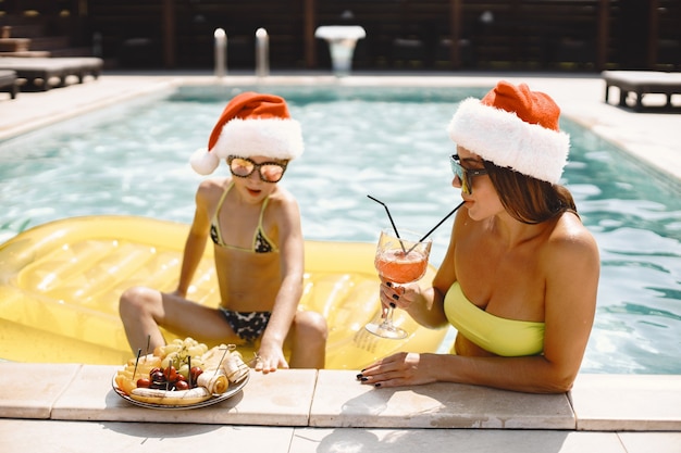 Moeder en haar kind in kerstmutsen bij het zwembad. Vakantie in exotisch land.