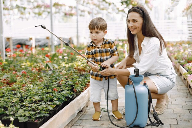 Moeder en haar zoon met een blauwe watersproeier in de kas. Kleine peuterjongen die bloemen water geeft in een kas