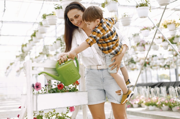 Moeder en haar zoon met een groene waterkan in de kas. kleine peuterjongen die bloemen water geeft in een kas