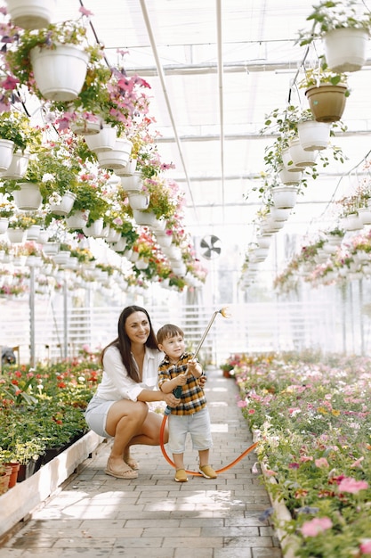 Moeder en haar zoon met een watersproeier in de kas. Kleine peuterjongen die bloemen water geeft in een kas