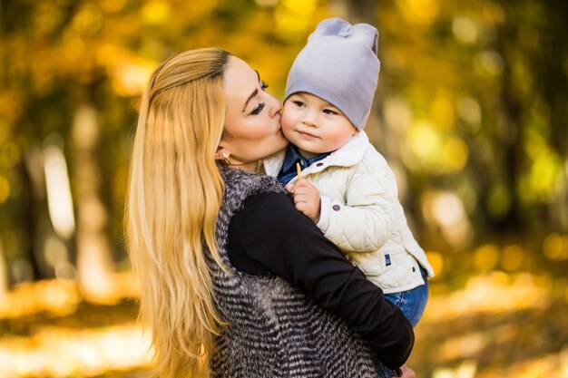 Moeder en haar zoon zijn in het herfstpark, de zoon kijkt graag naar zijn moeder, de vrouw houdt zijn handen vast