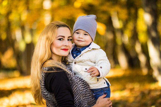 Moeder en haar zoon zijn in het herfstpark, de zoon kijkt graag naar zijn moeder, de vrouw houdt zijn handen vast