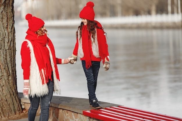 Moeder en kind in gebreide wintermutsen op familiekerstvakantie. Handgemaakte wollen muts en sjaal voor mama en kind. Breien voor kinderen. Brei bovenkleding. Vrouw en meisje in een park.