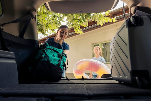 Moeder en klein meisje laden bagage in de kofferbak, reizen op zomervakantie reis. Opblaasbare en reistassen in de auto plaatsen om op avontuurlijke vakantie aan zee te vertrekken.