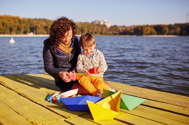 Moeder en zoon spelen met papieren boten aan het meer