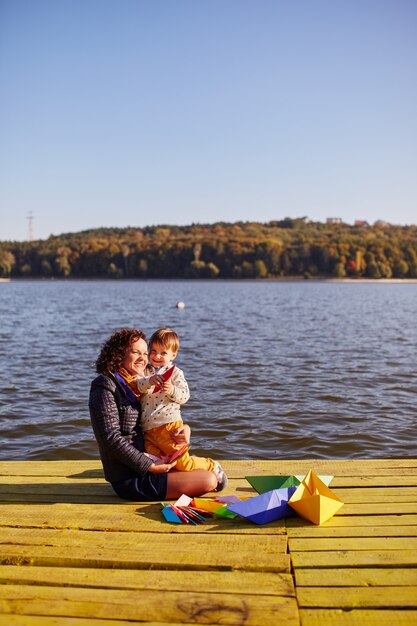 Moeder en zoon spelen met papieren boten aan het meer