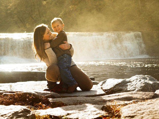 Moeder haar zoon knuffelen in een park omgeven door groen en een waterval in het zonlicht