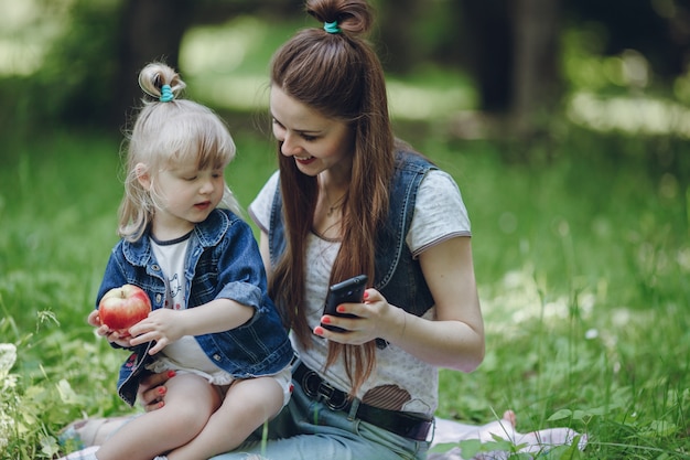 Moeder lachend terwijl haar dochter een appel eet en spelen met de mobiele