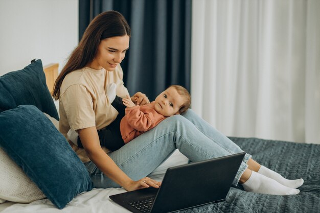 Moeder met babymeisje die thuis op de computer werkt