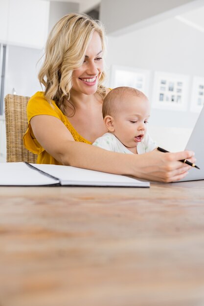 Moeder met behulp van laptop met baby jongen in de keuken