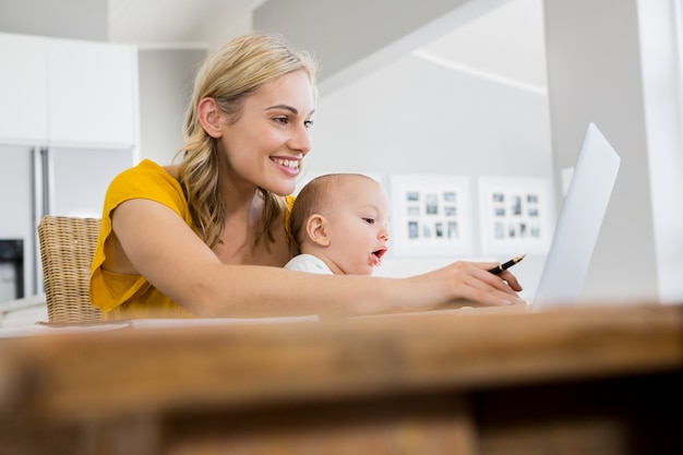 Moeder met behulp van laptop met baby jongen in de keuken