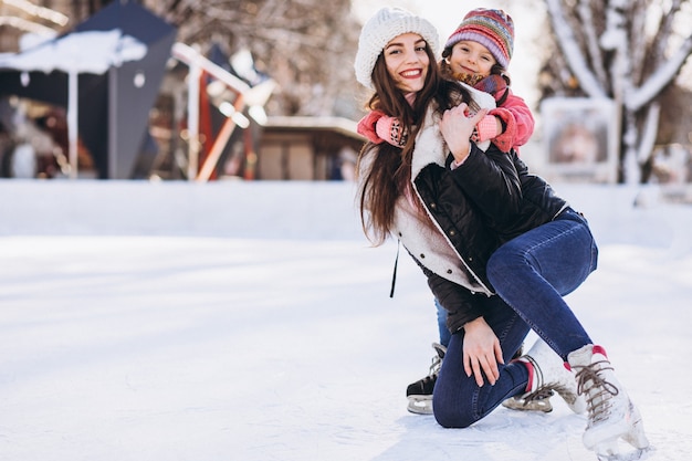 Moeder met dochter die het schaatsen op een piste onderwijzen