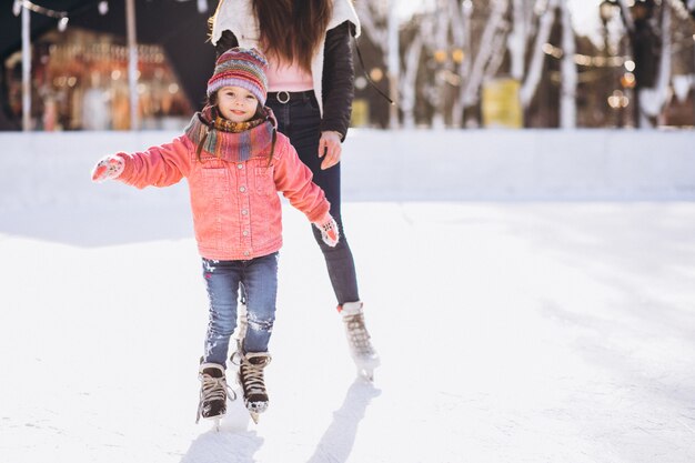 Moeder met dochter die het schaatsen op een piste onderwijzen
