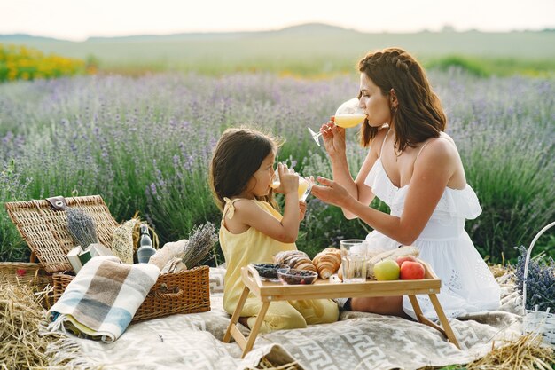 Moeder met dochtertje op lavendelveld. Mooie vrouw en schattige baby spelen in weide veld. Familie in een picknick.