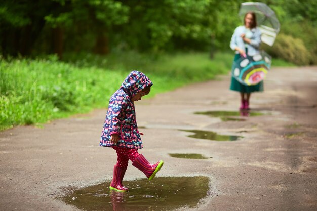 Moeder staat achter met paraplu&#39;s, terwijl haar dochter in poelen speelt na de regen