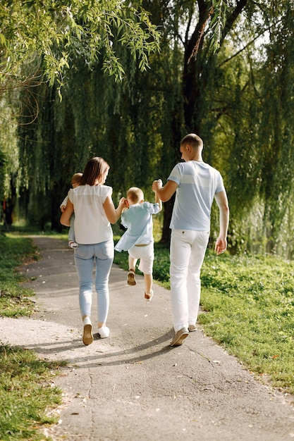 Moeder, vader, oudere zoon en kleine babydochter wandelen in het park. Familie in witte en lichtblauwe kleding