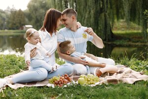 Moeder, vader, oudere zoon en kleine babydochter zittend op een picknickkleed in het park. familie in witte en lichtblauwe kleding
