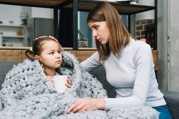 Moeder zorgt voor haar dochter bedekt met grijze wollen sjaal die lijdt aan koorts