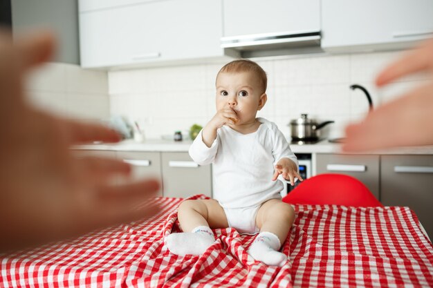 Moeders handen reiken om schattige baby zittend keukentafel te nemen