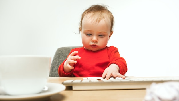 Moeilijke dag. kind babymeisje zit met toetsenbord van moderne computer of laptop in witte studio